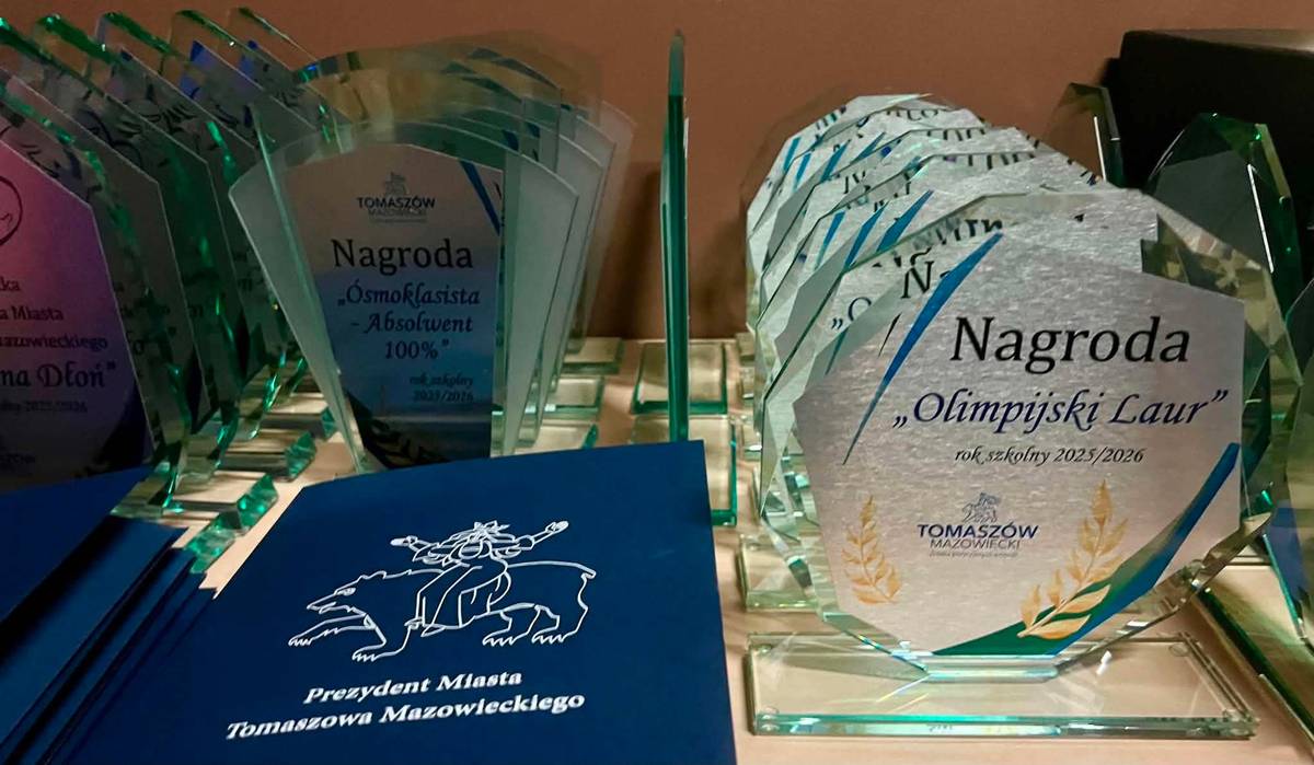 Ekspozycja nagród i dyplomów Prezydenta Miasta Tomaszowa Mazowieckiego dla szczególnie uzdolnionych uczniów.  Na stole leżą dyplomy oprawione w granatowe teczki z logotypem Miasta oraz stoją szklane statuetki m.in. Olimpijski Laur, Pomocna Dłoń.