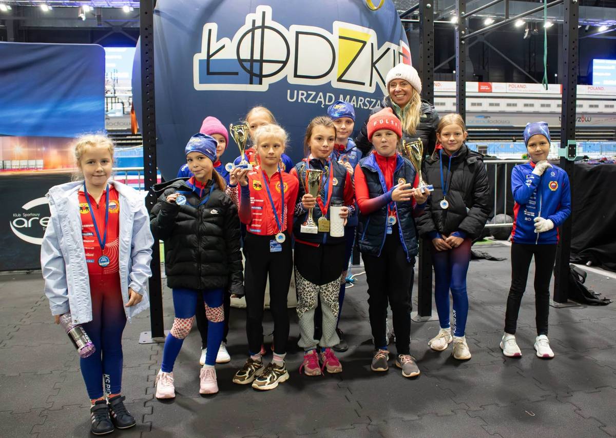 Na zdjęciu dzieci z medalami i pucharami zawodów Jeden lód - jedna pasja, które odbyły się w Arenie Lodowej. Dzieci pozują przy banerze Urzędu Marszałkowskiego w Łodzi