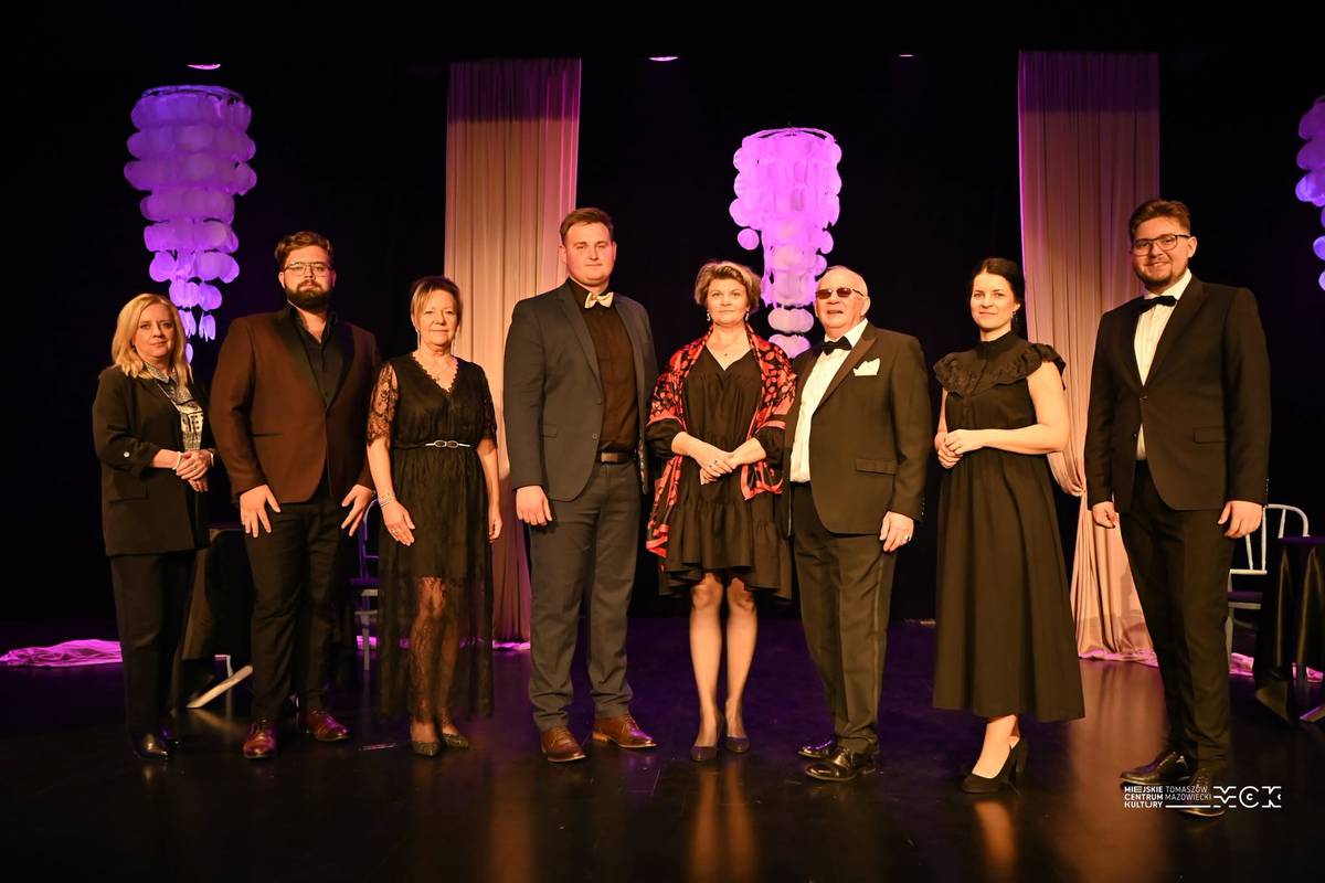 Na zdjęciu wykonawcy koncertu Grande Amore  w Miejskim Centrum Kultury Tkacz . Ubrani w eleganckie stroje, kobiety w czarne suknie, mężczyźni w garnitury, pozują do zdjęcia po zakończonym koncercie stojąc na scenie