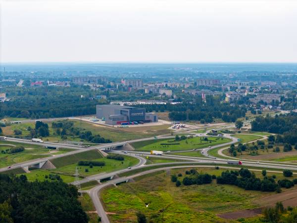 Zdjęcie z drona przedstawiające węzeł drogowy trasy S8 z wiaduktami i rondami, w tle hala magazynowa firmy Paradyż oraz zabudowa miejska Tomaszowa Mazowieckiego.