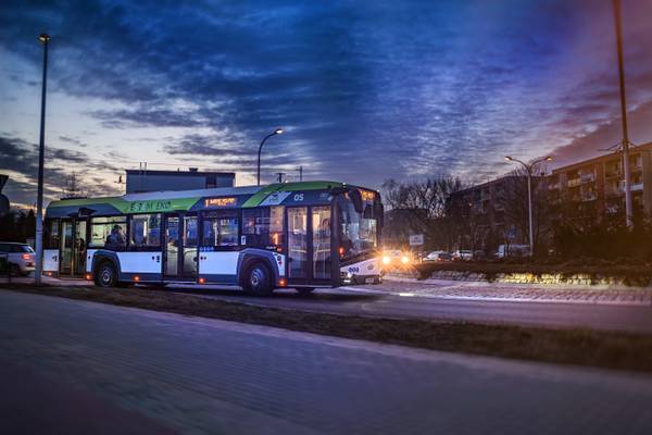 Miejski autobus hybrydowy marki Solaris z napisem „Jestem EKO zatrzymany na przystanku o zmierzchu.