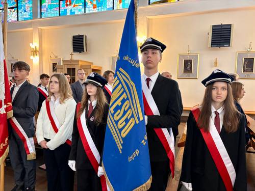 Poczty sztandarowe w kościele pw. NMP Królowej Polski przy ul. Słowackiego. Na pierwszym miejscu chorąży trzyma niebieski sztandar ze złotymi zdobieniami oraz napisem UNESCO. Obok stoją dziewczęta w galowych strojach i biało-czerwonych szarfach