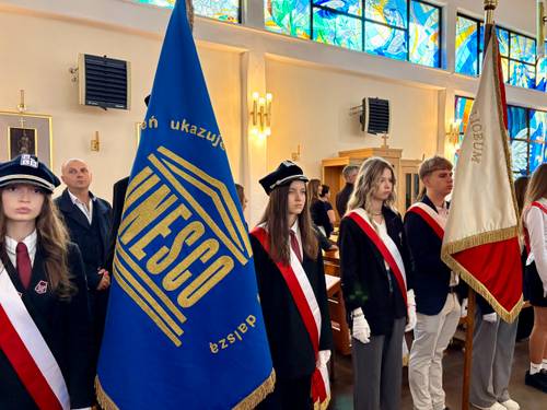 Poczty sztandarowe w kościele pw. NMP Królowej Polski przy ul. Słowackiego. Młodzież w galowych strojach i biało-czerwonych szarfach asystuje, trzyma sztandary na drzewcach. W tle uczestnicy obchodów