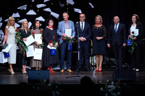 Na zdjęciu nagrodzeni dyrektorzy szkół z okazji Dnia Edukacji Narodowej, stoją na scenie z czerwonymi różami i dyplomami, obok stoją prezydent miasta i minister infrastruktury