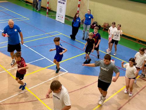 Trening ogólnorozwojowy z Olimpijczykiem Jaromirem Radke. Uczniowie ćwiczą w strojach gimnastycznych i słuchają wskazówek trenera. Zdjęcie wykonane z lotu ptaka