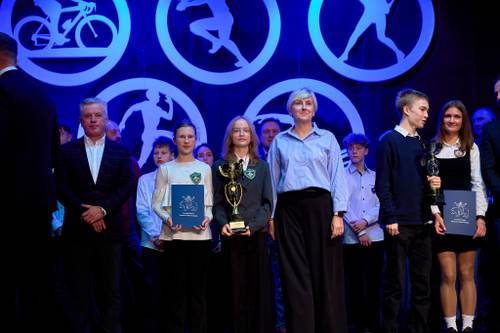 Laureaci współzawodnictwa sportowego, uczniowie i trenerzy z pucharami i dyplomami pozują na scenie