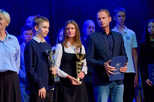 Laureaci współzawodnictwa sportowego, uczniowie i trenerzy z pucharami i dyplomami pozują na scenie