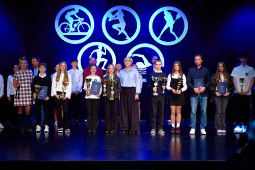 Laureaci współzawodnictwa sportowego, uczniowie i trenerzy z pucharami i dyplomami pozują na scenie