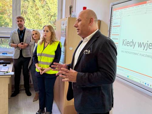 Prezydent miasta i dyrektor szkoły omawiają organizację i przebieg ćwiczeń. W tle tablica edukacyjna z rodzajami alarmów
